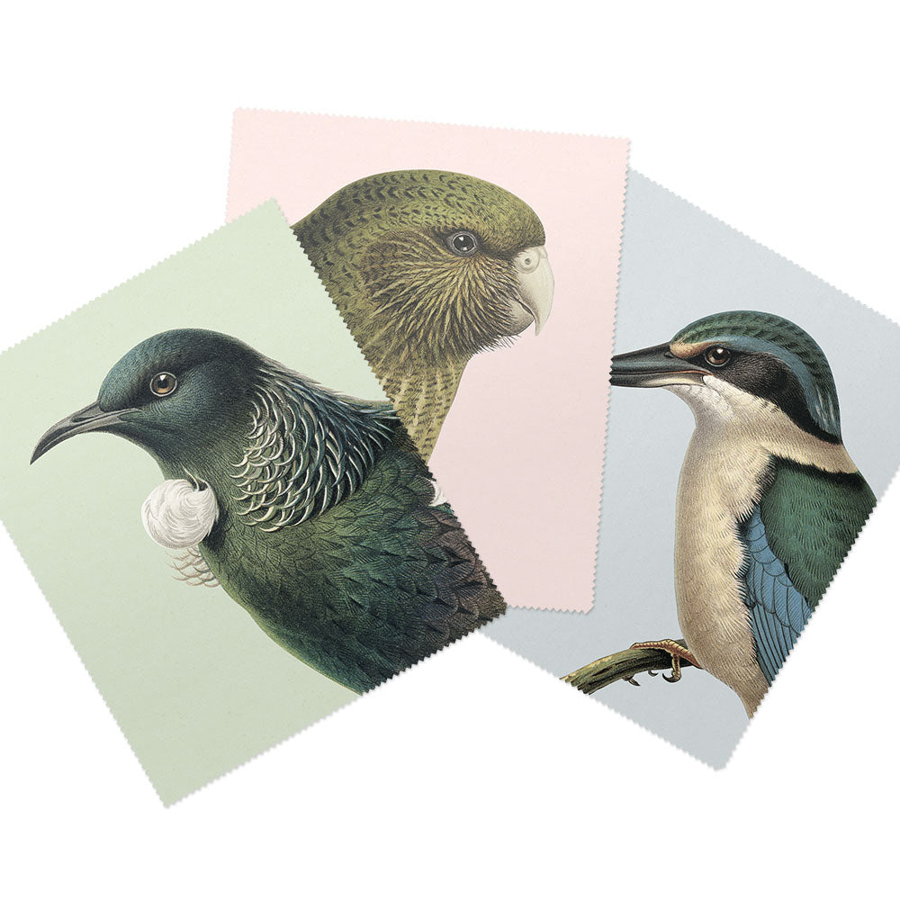 The Set of 3 Hushed Collection Lens Cloths features a green kākāpō on pink, a black-and-white tūī on pale green, and a blue-breasted kingfisher on light gray—each with unique New Zealand bird illustrations.