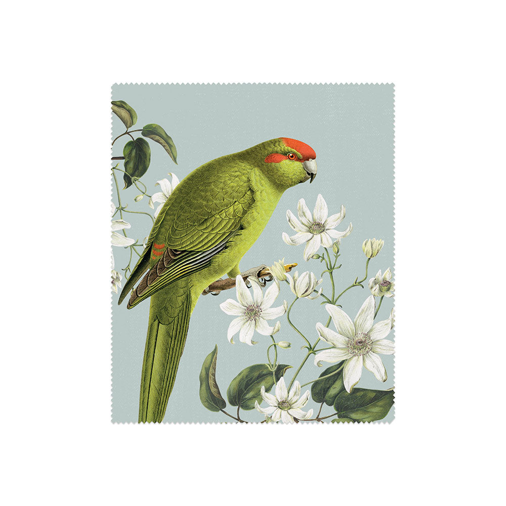 Part of the Set of 3 Birds & Botanicals Collection Lens Cloths, this cloth features a green parrot with a red stripe on its head perched on a branch with white flowers and leaves against a pale blue background.