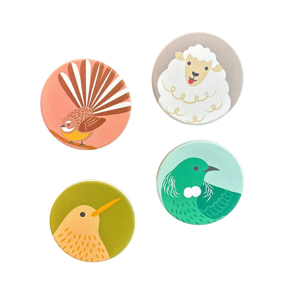 The Storybook Ceramic Magnet Set features four circular magnets: a bird with a fanned tail on pink, a white sheep on beige, a green bird on light blue, and a yellow bird on green—printed in New Zealand.