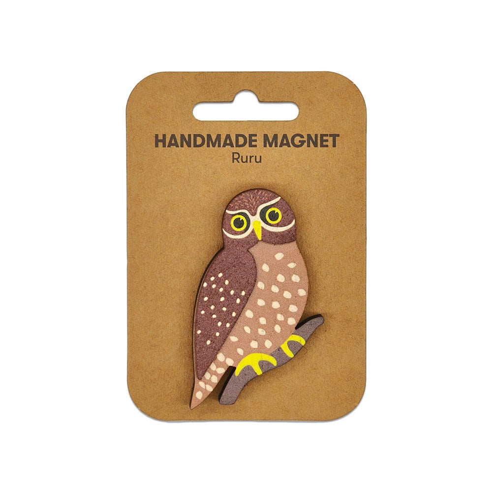 The Ruru Wooden Magnet is a handcrafted, owl-shaped Kiwiana design with yellow and brown details. It features large yellow eyes, perched on a branch, and comes attached to a brown card labeled HANDMADE MAGNET Ruru.