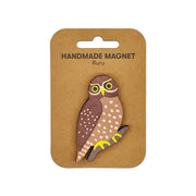 The Ruru Wooden Magnet is a handcrafted, owl-shaped Kiwiana design with yellow and brown details. It features large yellow eyes, perched on a branch, and comes attached to a brown card labeled HANDMADE MAGNET Ruru.