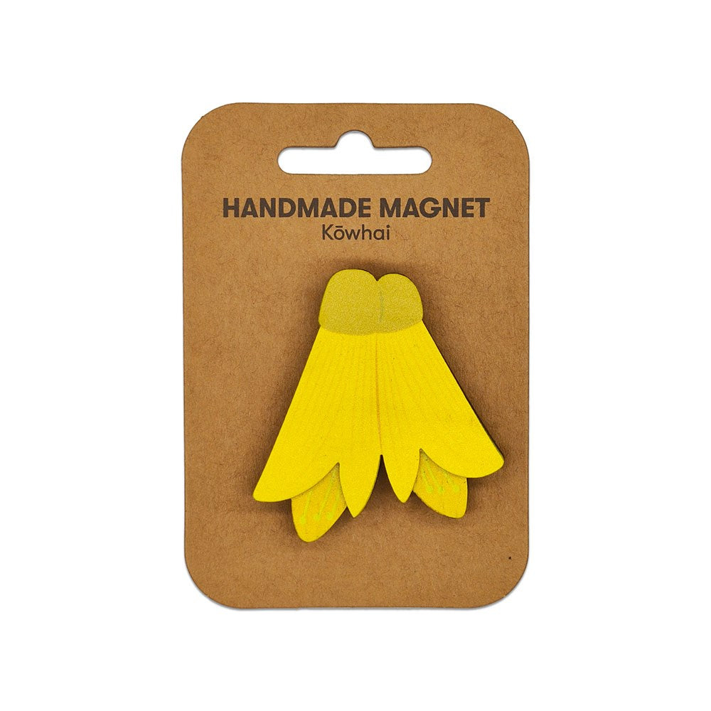A Kowhai Wooden Magnet with a yellow design is attached to a brown card labeled Handmade Magnet Kōwhai on a white background, making it a charming Kiwiana piece for your collection.
