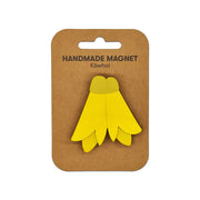 A Kowhai Wooden Magnet with a yellow design is attached to a brown card labeled Handmade Magnet Kōwhai on a white background, making it a charming Kiwiana piece for your collection.