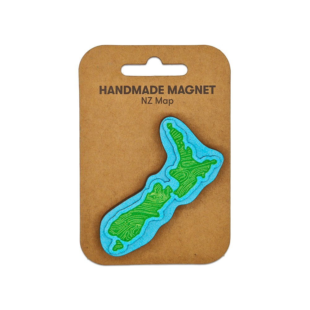 The NZ Map Wooden Magnet is a handmade fridge magnet shaped like New Zealand, with green land and blue water details, mounted on a brown card labeled Handmade Magnet NZ Map.