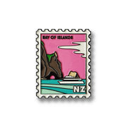 The Bay of Islands Collectible Stamp Magnet by Glenn Jones features a cruise ship on blue water near cliffs and greenery, with a pink sky and white clouds. BAY OF ISLANDS appears at the top and NZ at the lower right.