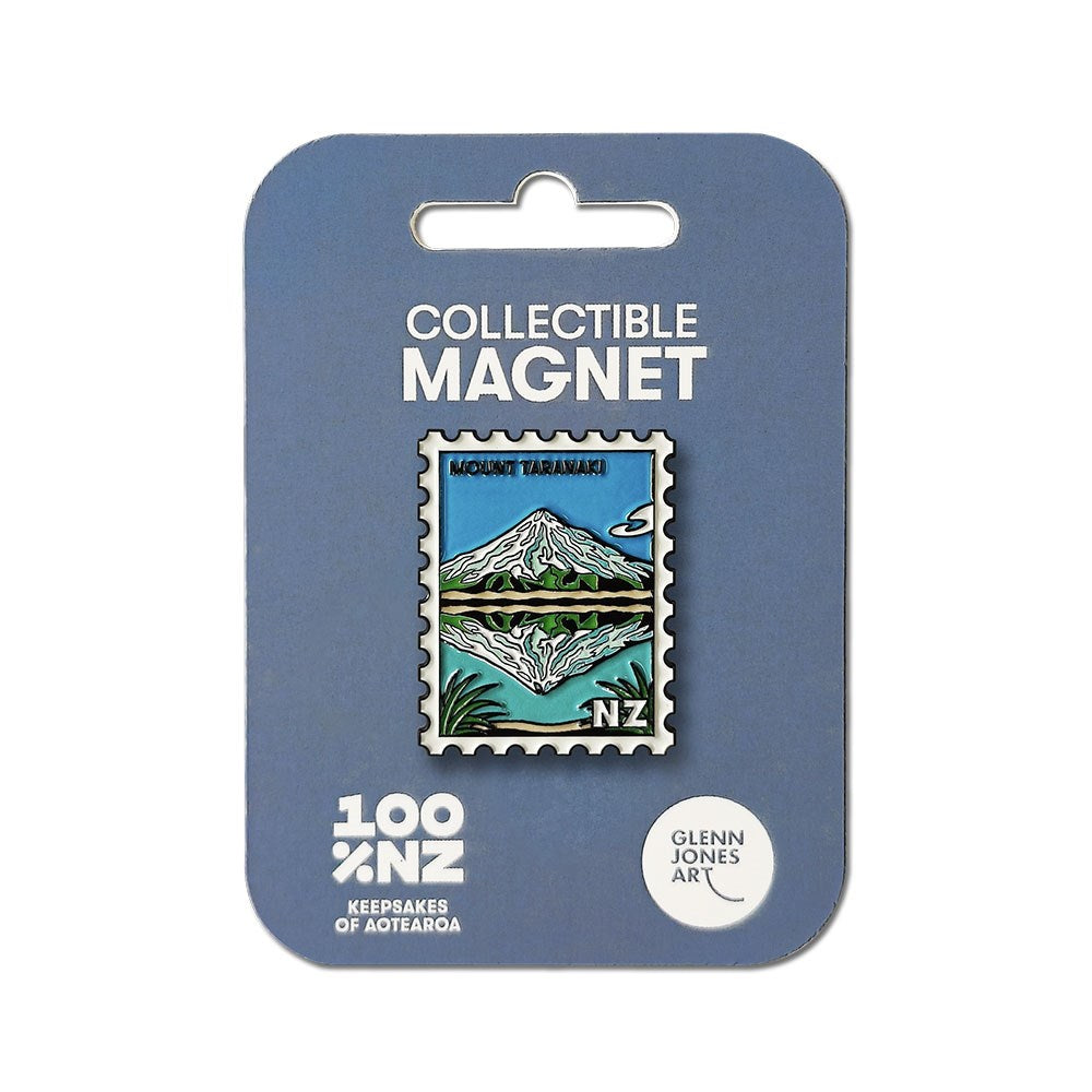 The Mt Taranaki Collectible Stamp Magnet features Glenn Jones’s illustration of Mount Taranaki on a postage stamp–shaped enamel magnet, set against a blue sky and green landscape, packaged on blue backing labeled Collectible Magnet.