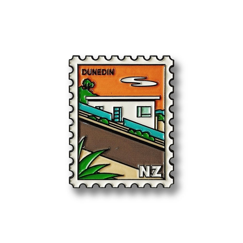 A Dunedin Collectible Stamp Magnet featuring a modern white house on a sloped, green street. Showcases Glenn Jones Artwork and New Zealand Design, with DUNEDIN at the top and NZ at the bottom right on an orange background.