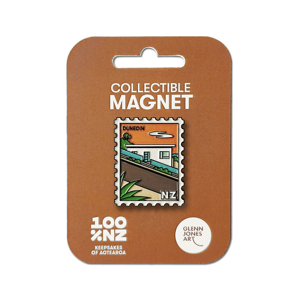 The Dunedin Collectible Stamp Magnet features Glenn Jones artwork of a house with Dunedin text, shaped like a postage stamp and displayed on brown packaging labeled Collectible Magnet and 100% NZ Keepsakes of Aotearoa.