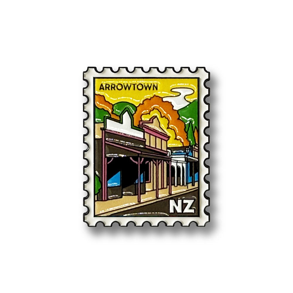The Arrowtown Collectible Stamp Magnet features an illustration of historic buildings in Arrowtown, New Zealand, set against vibrant clouds and lush greenery. The design includes the letters "NZ" in the bottom right corner, making it a charming keepsake to celebrate local heritage—perfect as a collectible enamel stamp or an Arrowtown souvenir magnet.