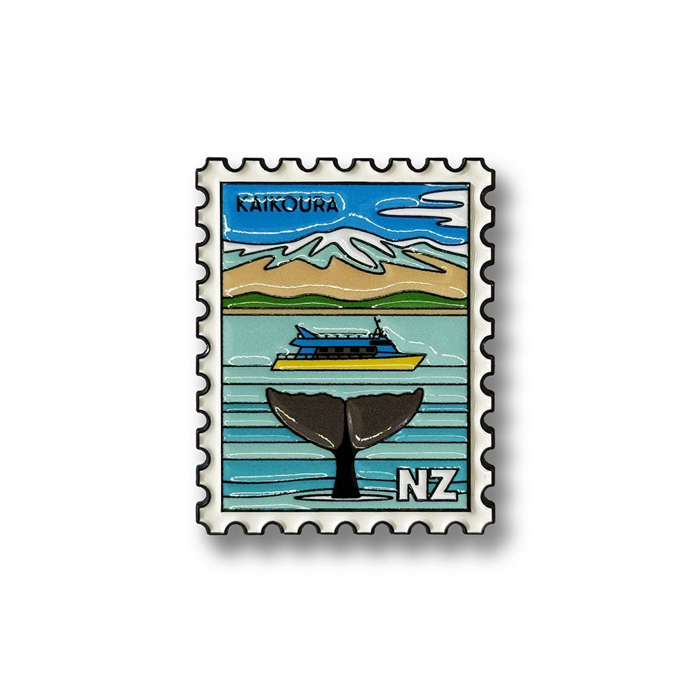The Kaikora Collectible Stamp Magnet showcases Glenn Jones artwork, featuring an illustrated whale's tail in the ocean, a boat, mountains, and "Kaikoura" at the top. With bold lines and vibrant colors, this enamel magnet also displays "NZ" in the corner to represent New Zealand.