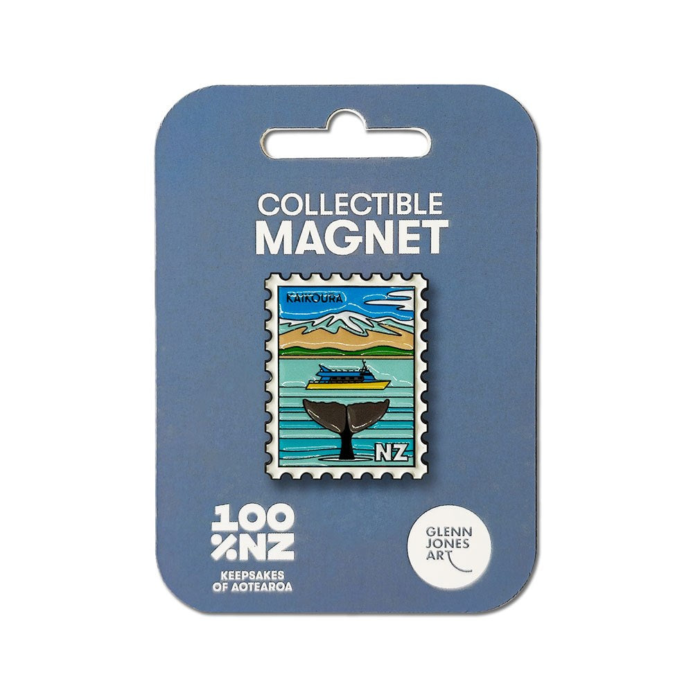 The Kaikora Collectible Stamp Magnet is a uniquely designed enamel magnet in the shape of a postage stamp, featuring Glenn Jones's artwork of a whale tail splashing against a backdrop of mountains. The magnet displays "Kaikoura" and "NZ," and comes attached to a blue backing card labeled "Collectible Magnet.