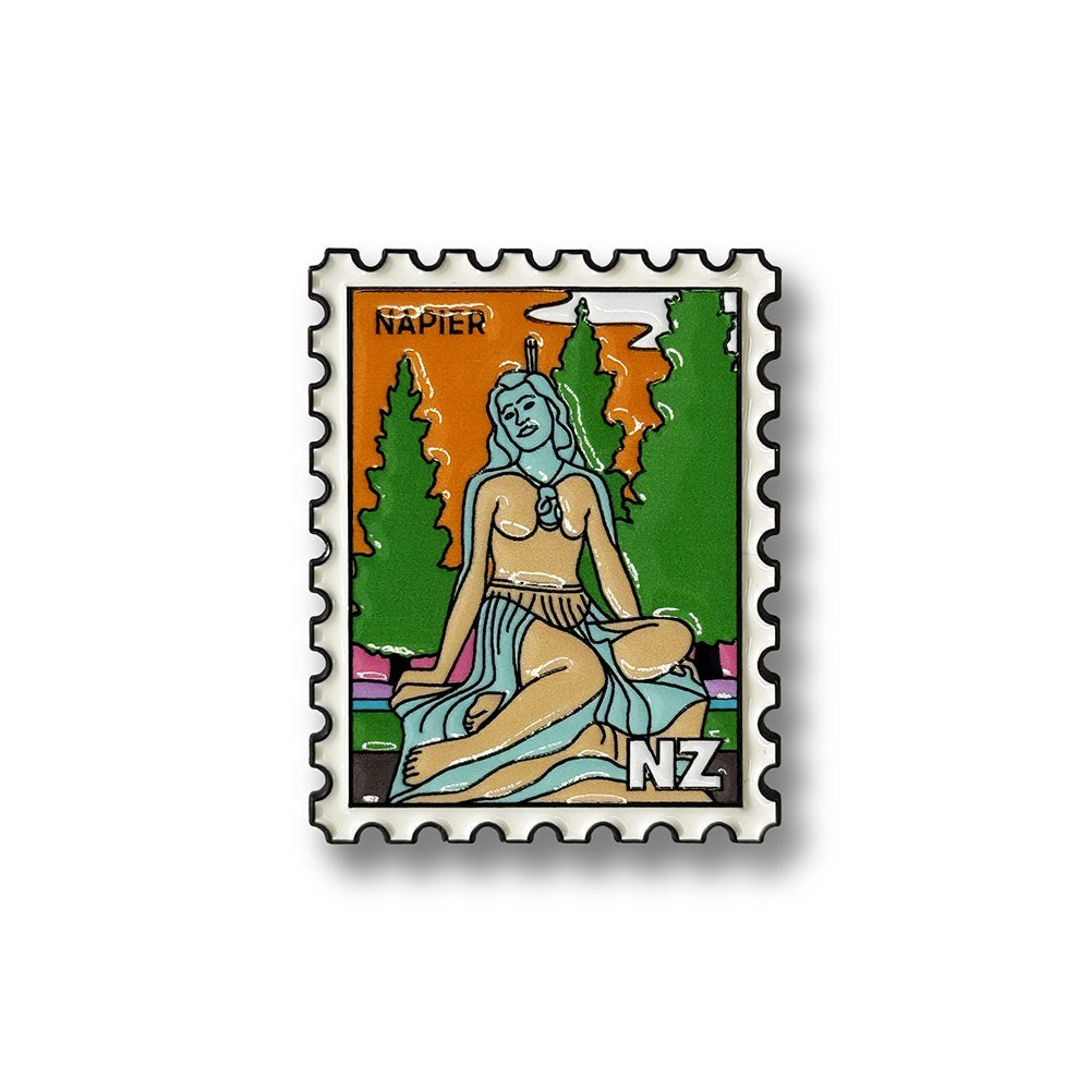 A collectible enamel magnet shaped like a postage stamp, featuring a stylized woman in a skirt sitting on grass with trees and a sunset in the background. The magnet has “Napier” at the top and “NZ” at the bottom right, celebrating the charm of New Zealand. Product: Napier Collectible Stamp Magnet.