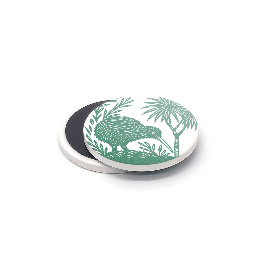 The Woodcut Ceramic Magnet Set features a round white ceramic magnet with a green kiwi bird by a small tree. Perfect as a New Zealand souvenir, this charming piece reveals its black magnetic backing beneath the printed ceramics.
