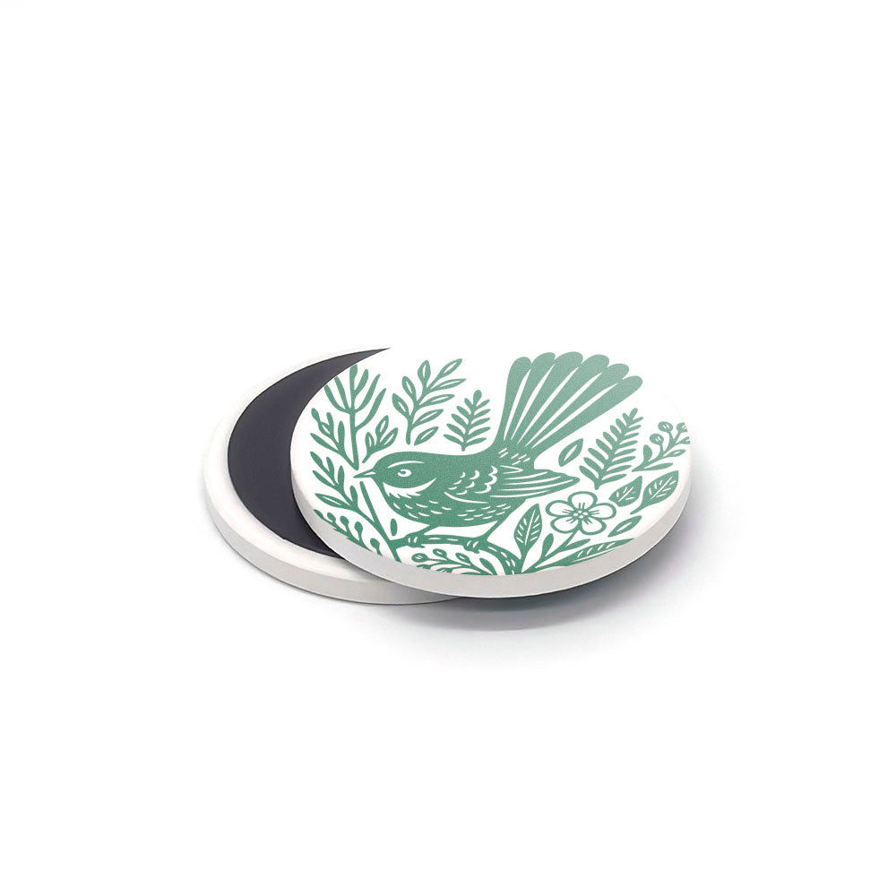 The Woodcut Ceramic Magnet Set features a round white ceramic magnet with a green bird among leaves and flowers. Its black back is visible against a white background—ideal for unique New Zealand souvenirs or printed ceramics lovers.