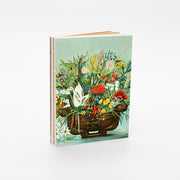 The NZ Native Flowers Notebook is a stylish art notebook with exposed binding, featuring a cover illustration of a woven basket filled with colorful native flowers against a light background.