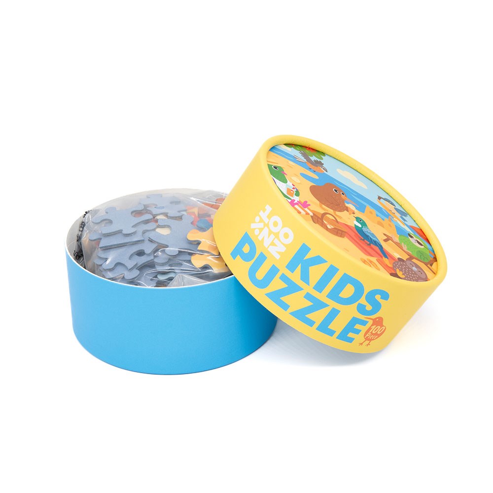 A round yellow and blue box labeled “Beach Party Kids Puzzle” sits open, showing loose jigsaw pieces. The lid displays bright animal and nature illustrations, making it a delightful New Zealand puzzle for children.
