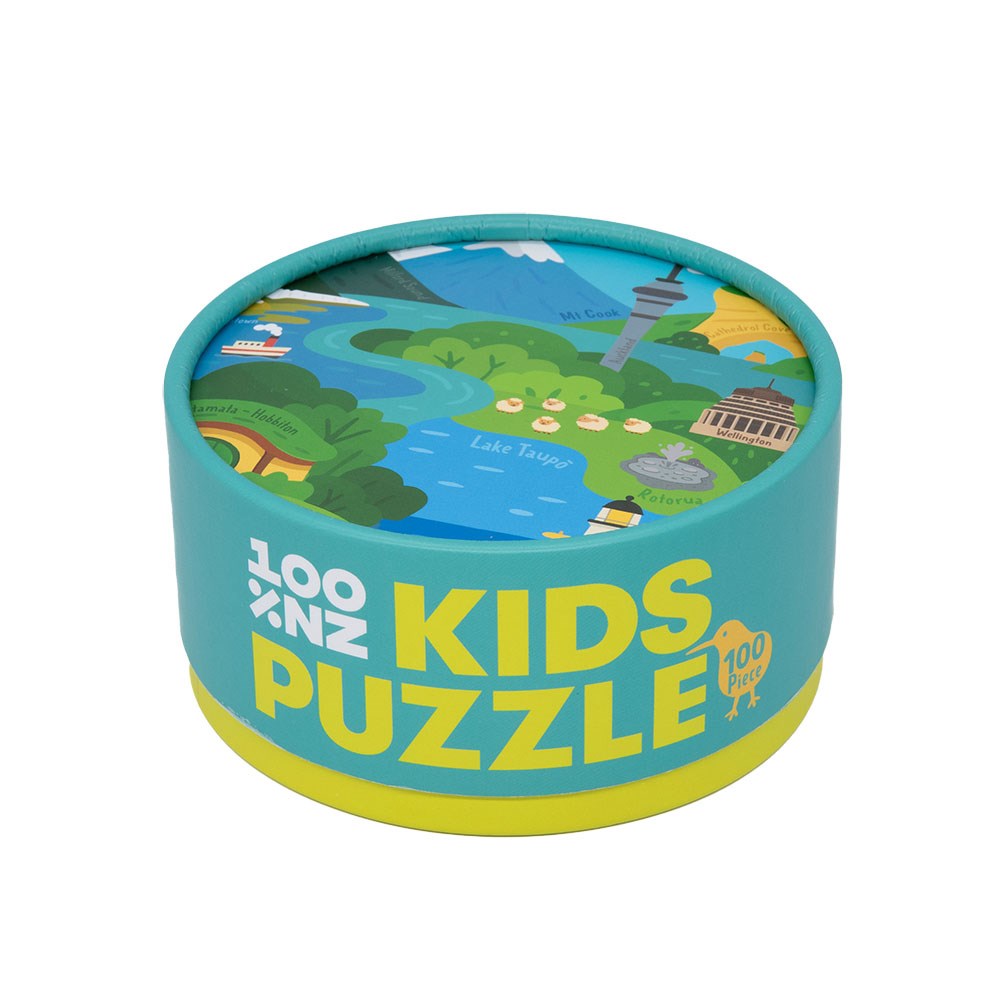 A mostly teal, round box with a yellow base labeled "NZ Highlights Kids Puzzle" in bold yellow and white. The lid features an illustrated map scene of New Zealand; the box contains a vibrant 100 piece puzzle.