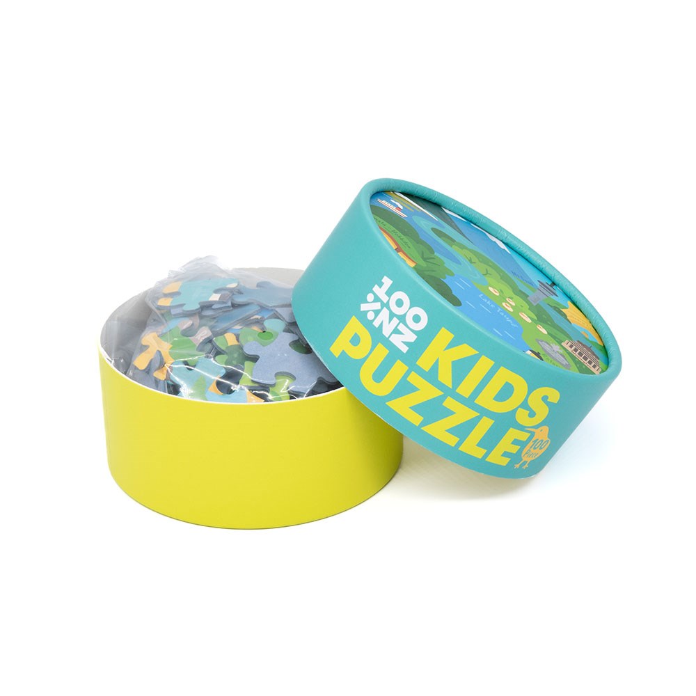 A round box labeled “NZ Highlights Kids Puzzle” with a partially removed lid reveals colorful pieces inside. The yellow and teal box features playful graphics, perfect for kids who enjoy 100-piece puzzles.