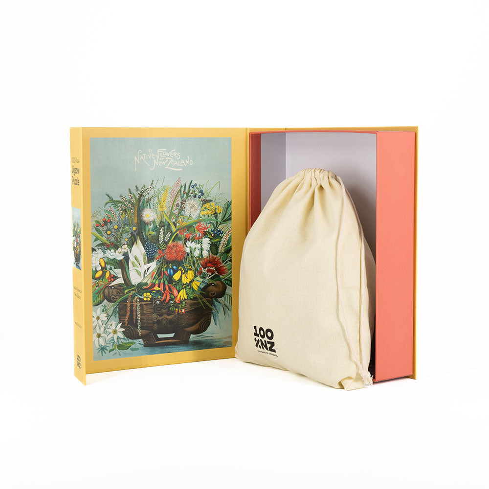 The NZ Native Flowers Jigsaw Puzzle features a yellow box with an illustrated floral inner cover, a beige drawstring bag labeled 100 PANZ inside, and a white background, beautifully inspired by New Zealands native flowers.