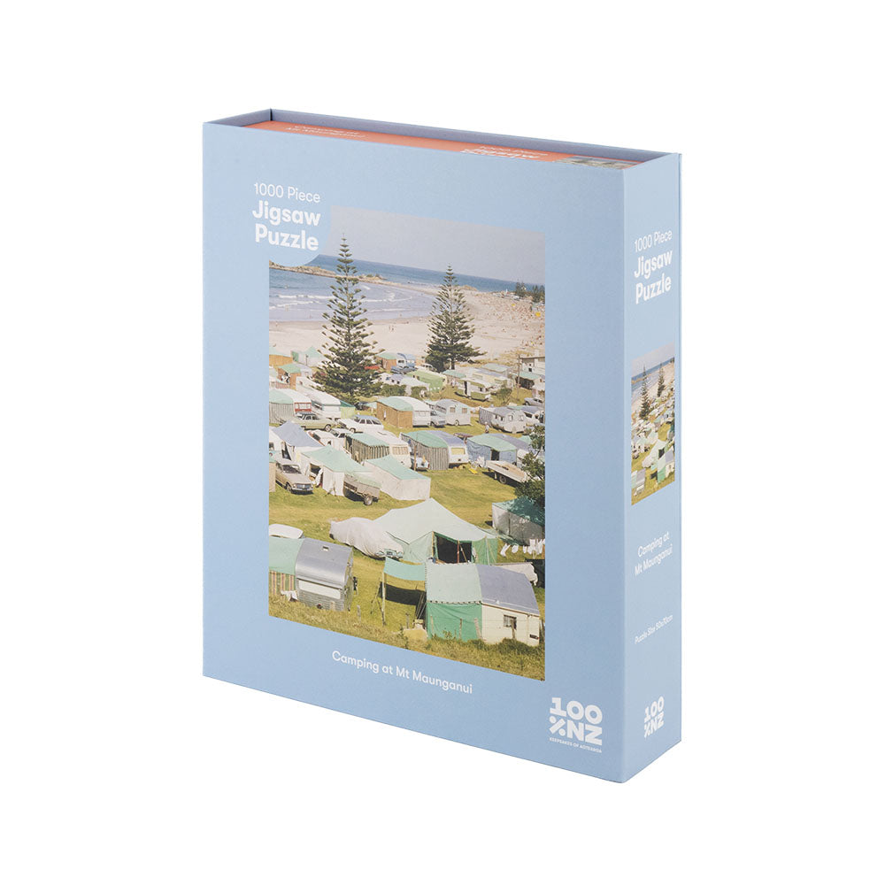 Enjoy camping nostalgia with the 1000-piece Camping at Mt Maunganui Jigsaw Puzzle, featuring a scenic campground near the beach and trees. The light blue box reads: Camping at Mt Maunganui, 1000 Piece Jigsaw Puzzle.