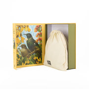The Botanical Tui Jigsaw Puzzle Box features a yellow exterior, an inner cover with birds and flowers, and includes a partly visible drawstring bag printed with 100 NZNZ—perfect for New Zealand bird puzzle fans.