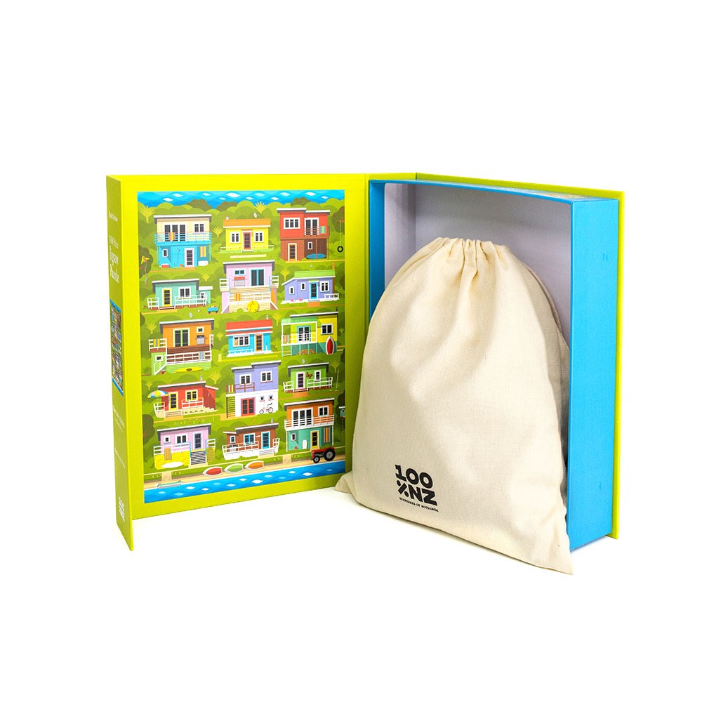 An open Glenn Jones - Kiwi Cribs & Baches Jigsaw Puzzle box, featuring coastal house art, reveals a beige drawstring bag with a partly visible “ZOO” logo in the right compartment.