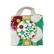 The Bright Manuka Shopping Bag is an affordable, reusable shopping bag with a floral design in white, green, yellow, and pink. It features short beige handles and a label that reads “Shopping Bag, Mānuka, 100% NZ.”.