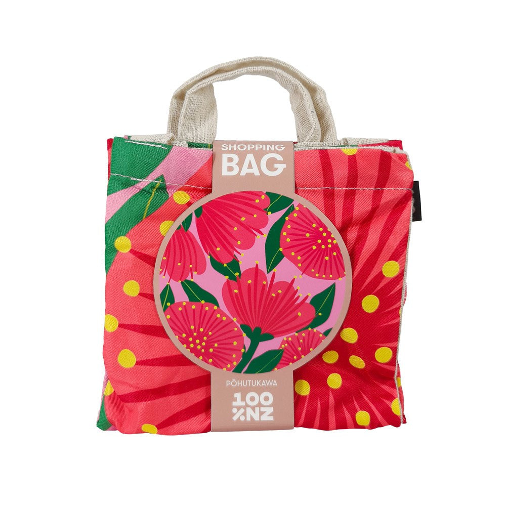 The Bright Pink Pohutukawa Shopping Bag is a foldable, affordable reusable bag with a vivid red, pink, yellow, and green floral design. The packaging says “SHOPPING BAG” and highlights a close-up illustration of the pohutukawa flower.