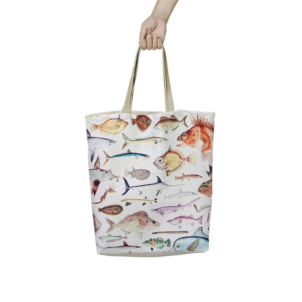 A hand holds the lightweight, reusable Fishes of New Zealand Shopping Bag, featuring colorful fish illustrations on the front, against a plain white background.