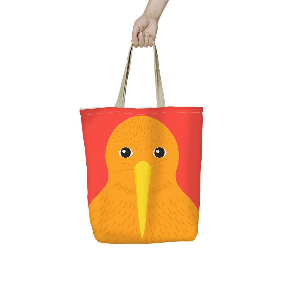 A hand holds the Bright Kiwi Shopping Bag, featuring beige handles and a red background with a cartoon orange kiwi bird sporting a long yellow beak and round black eyes.