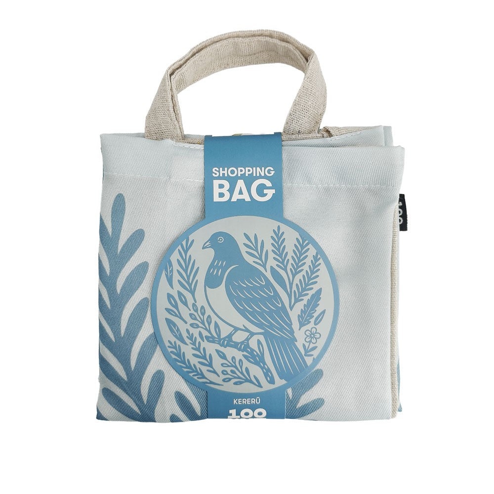 Woodcut Kereru Shopping Bag, an off-white reusable bag featuring a blue circular graphic of a kererū bird and foliage, held together by a paper tag.