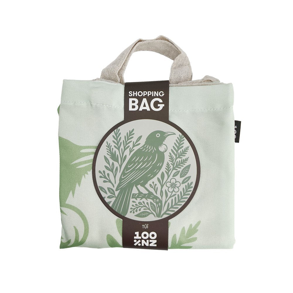 A folded light green Woodcut Tui Shopping Bag featuring a brown paper band with a woodcut-style Tui bird illustration and the text Shopping Bag and 100% NZ.
