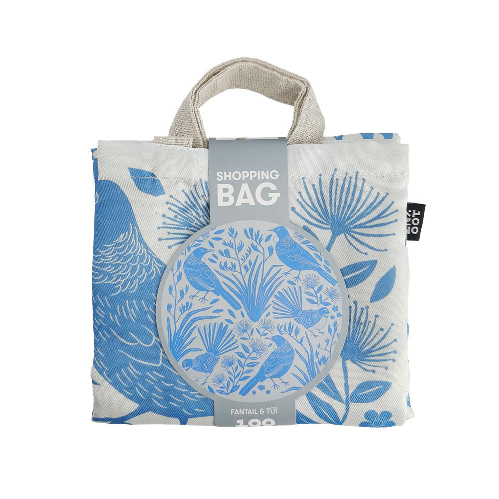 Birdsong Blues Shopping Bag, a folded, lightweight bag featuring a blue and white pattern of fantail birds and flowers, with a paper bellyband that reads Shopping Bag and Fantail & Tūī.
