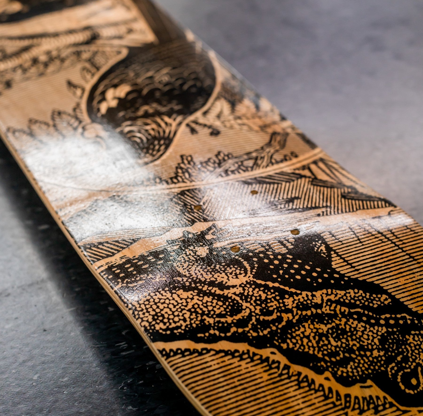 A close-up of the Tuatara Stamp Skateboard Deck, crafted from Canadian maple with an intricate black and tan engraved design, rests on a dark reflective surface—ideal as a striking piece of contemporary art.