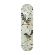 The Chatty Fantails Skateboard Deck features a contemporary illustration of two birds with yellow and brown bodies, accented by black and white, perched on flowering branches against a pale green background. Made from Canadian maple.