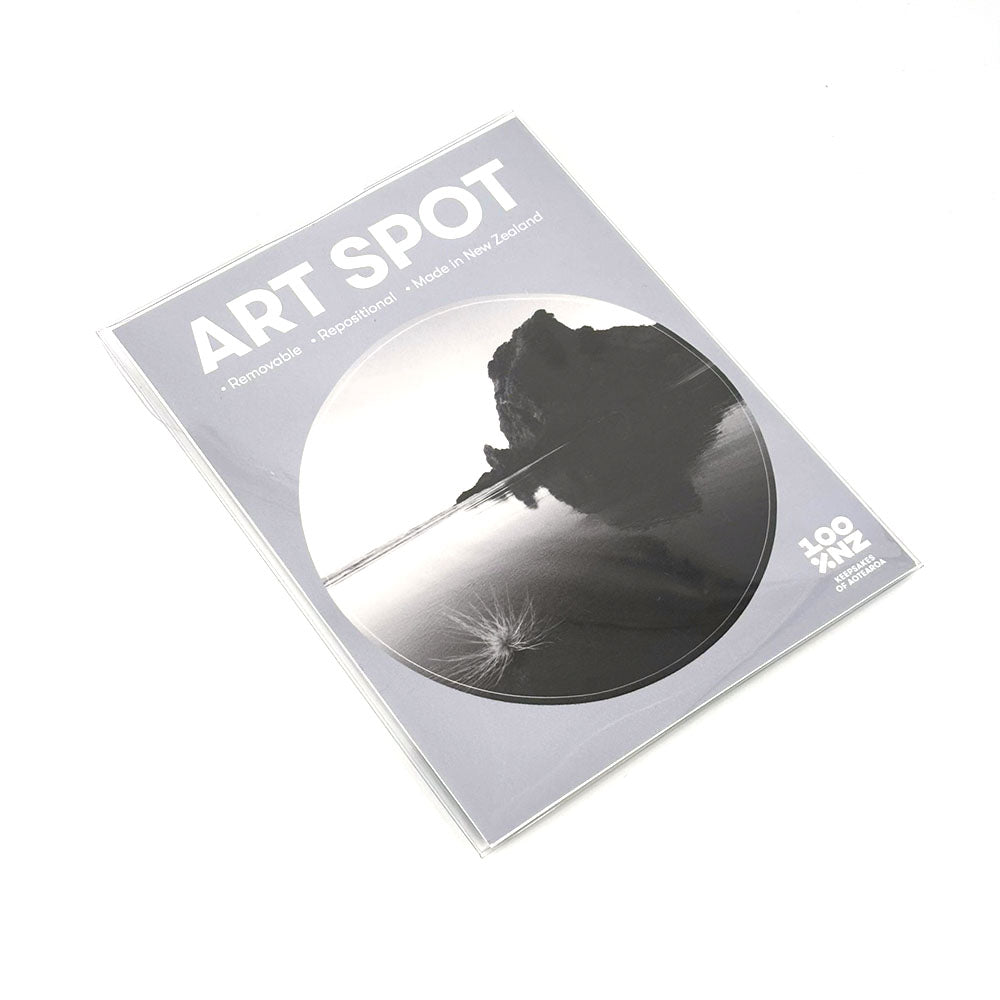 The Piha Art Spot is a sealed package featuring a black and white landscape photo of water and rock formations. Made in New Zealand, this repositionable wall art has a matte fabric finish and uses unique adhesive for easy application.