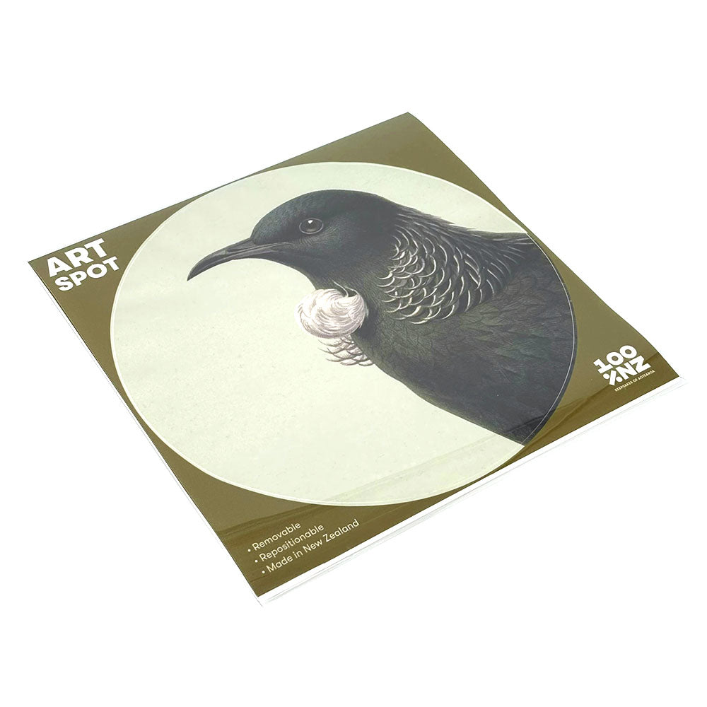 The Hushed Green Tui Art Spot is a square booklet featuring a matte fabric cover with a black bird and white neck tuft on a light background. This 100% NZ repositionable wall art uses unique adhesive for easy display.
