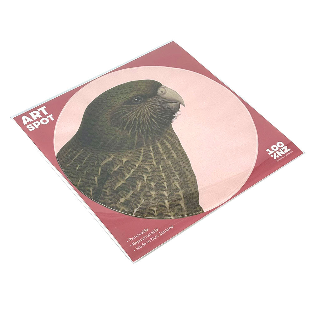 The Hushed Pink Kakapo Art Spot is a square art print with a green parrot on a pink circular background. Made in New Zealand, it features a matte fabric finish and is repositionable, removable, and reusable wall art.