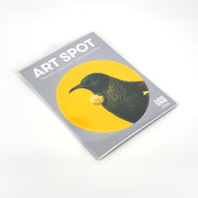 Bright Tui Art Spot is a packaged art print featuring a bird with green and gold plumage on a yellow circle. The peel-and-stick packaging highlights it as removable, repositionable wall art made in New Zealand.