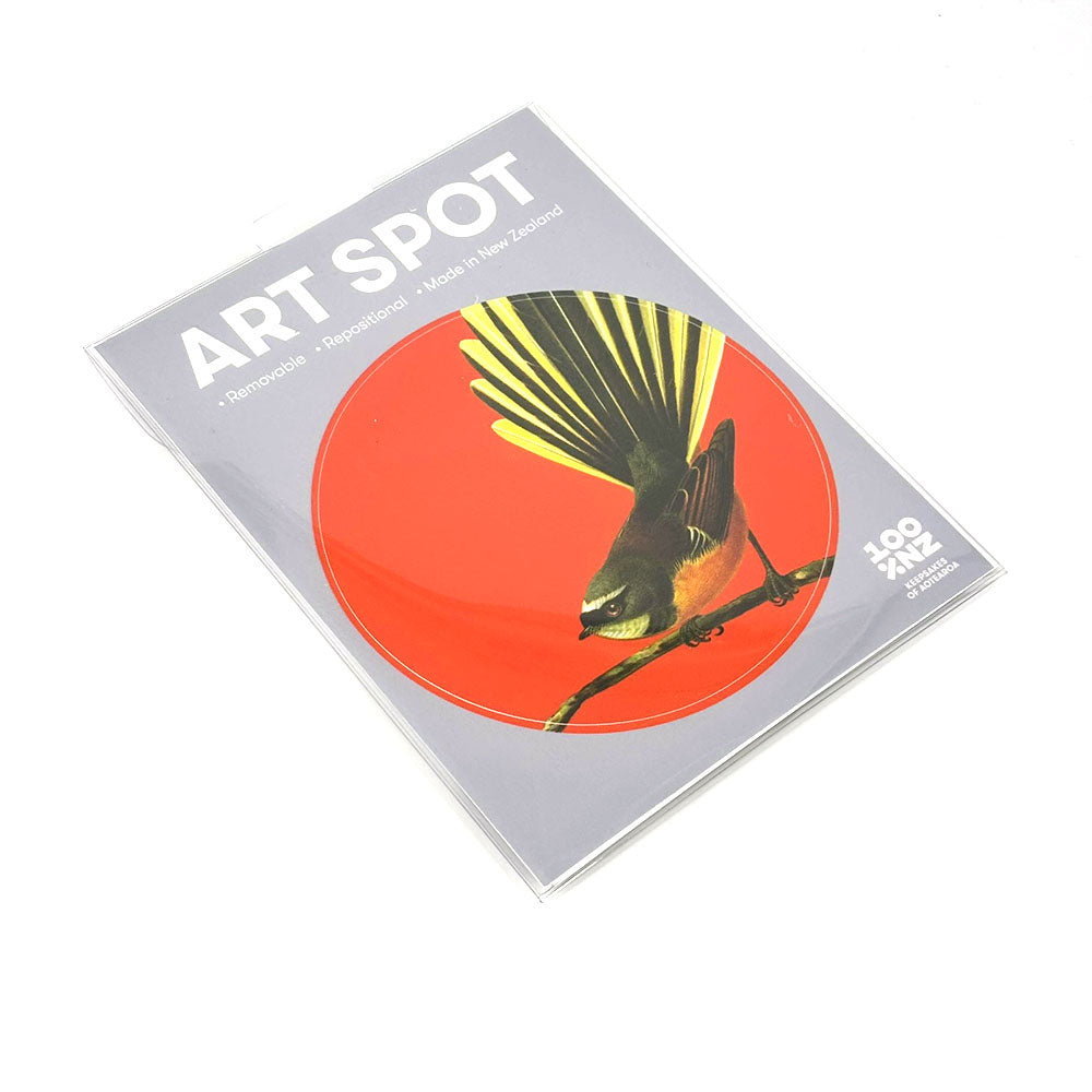 The Bright Fantail Art Spot is a round, repositionable wall art print showing a bird with a fanned tail on a branch, set against a bright red background. It has a matte fabric finish, comes in ART SPOT packaging, and is made in New Zealand.