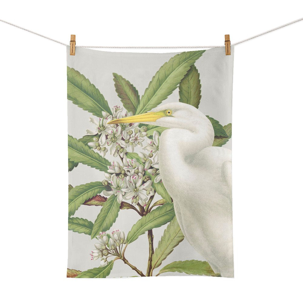 The Birds & Botanicals Heron Tea Towel, made in New Zealand, features a white heron among green leaves and white flowers, and is shown hanging with wooden clothespins.