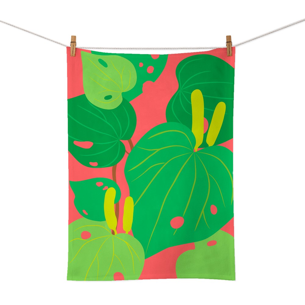 The Bright Botanical Kawakawa Tea Towel, made of cotton with large green leaves and yellow stems on a coral pink background, hangs from a clothesline—ideal for bringing a vibrant touch of New Zealand to your kitchen.