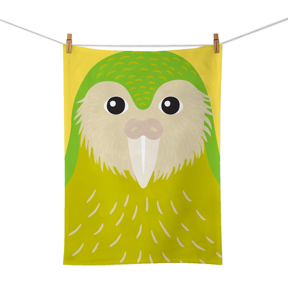 The Bright Kakapo Tea Towel, featuring a vibrant yellow and green cotton design with a stylized kakapo illustration, hangs on a clothesline with two wooden clothespins against a white background.