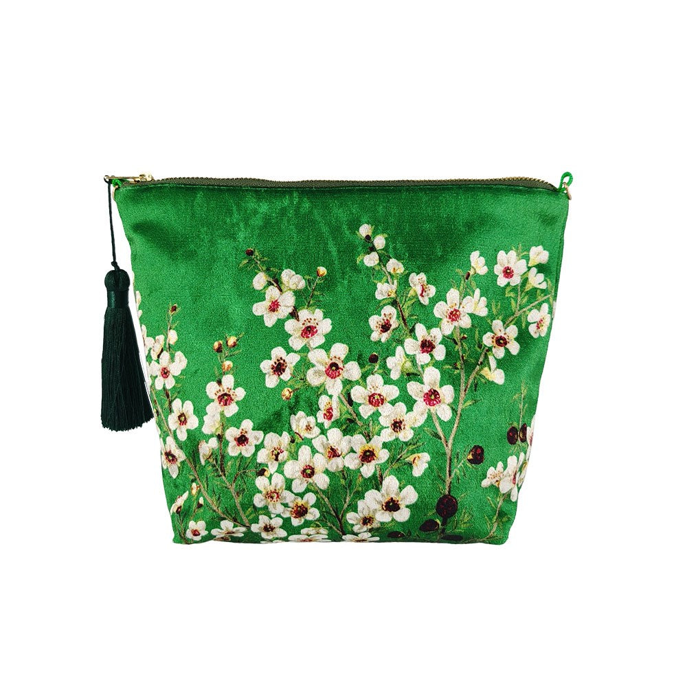 The Manuka Flower Velvet Cosmetic Bag is a green zippered pouch with a dark green tassel, embroidered white and pink Manuka flowers, and green leaves, inspired by New Zealand’s floral beauty.