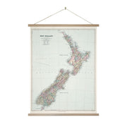 The Map of New Zealand Wall Chart features a vintage-style display of the North and South Islands with labeled regions, cities, and major landmarks in a wooden frame with hanging string. Made in New Zealand.