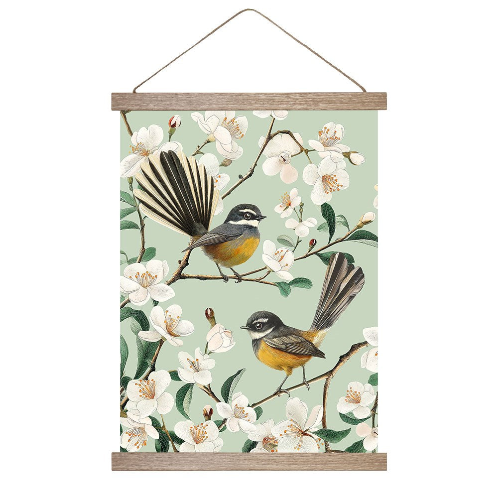 The Chatty Fantails Wall Chart features two yellow-chested fantail birds with long tails on blossoming branches against a light green background, framed with wooden bars and hung by a string for instant wall art display.