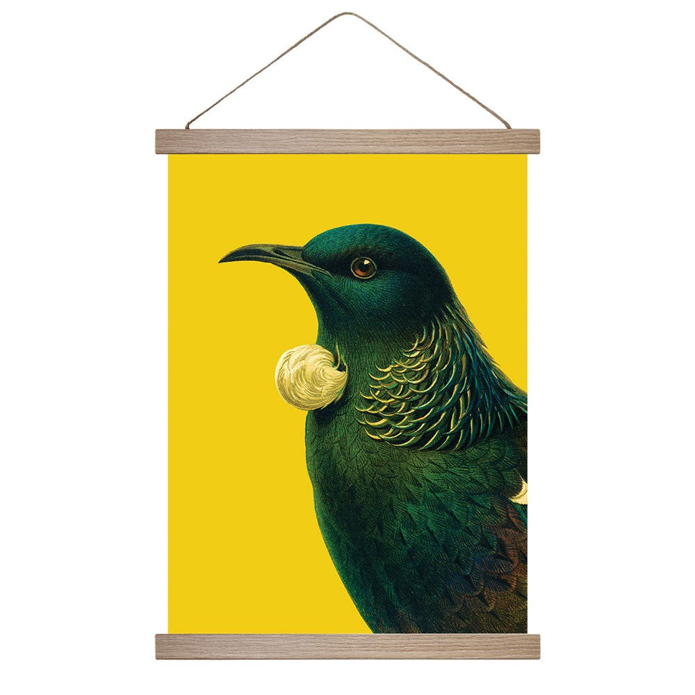 The Bright Tui Wall Chart features a tui bird with dark green-blue feathers and a white throat tuft on a vivid yellow background. Ready to hang with wooden bars, this artwork is proudly made in New Zealand.