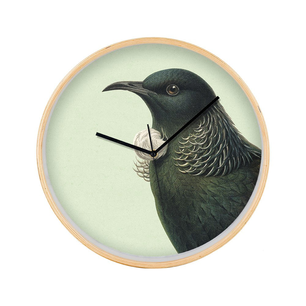 The Hushed Green Tui Wooden Frame Clock features a pale green background with an illustration of a native New Zealand Tui. Its black hour and minute hands point to 11 and 2, with the second hand at 12.