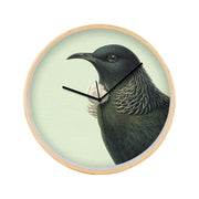 The Hushed Green Tui Wooden Frame Clock features a pale green background with an illustration of a native New Zealand Tui. Its black hour and minute hands point to 11 and 2, with the second hand at 12.