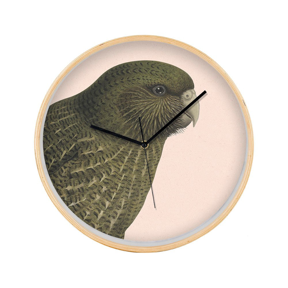 The Hushed Pink Kakapo Wooden Frame Clock features a light wooden frame, a Kakapo illustration on its face, black hands, silent movement, and a numberless round design for a clean, modern look inspired by New Zealands native bird.